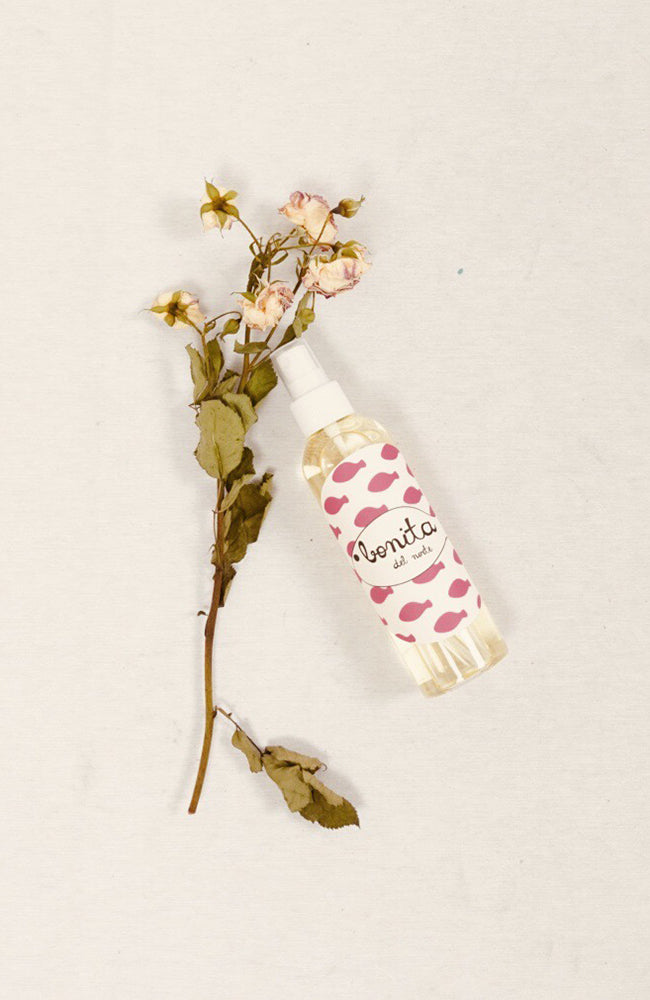 Una botella de spray de ambientador y una flor seca sobre una superficie.